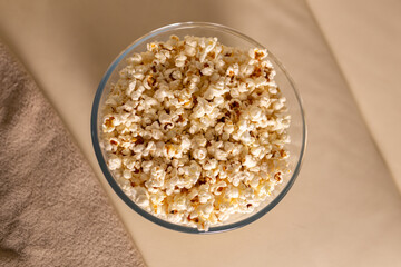 Bowl of popcorn for watching a film on a beige couch. Snacks and unhealthy junk food concept