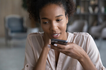 Focused young attractive brazilian african american woman recording audio message on smartphone,...