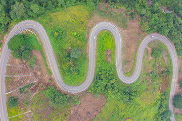Aerial view of cars driving on curved, zigzag curve road or street on mountain hill with green...