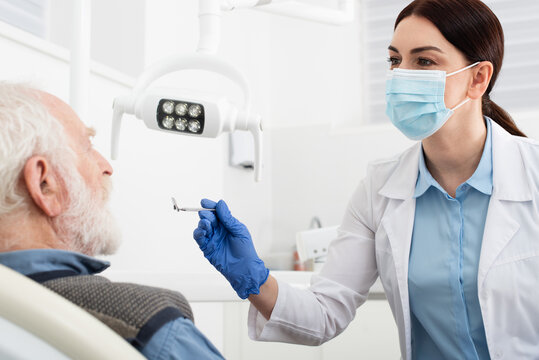 senior man having teeth examination by dentist in latex gloves with mirror in dental chair.
