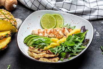 Healthy vegetable buddha bowl lunch with grilled chicken breast, halloumi, pineapple, avocado, green rocket salad, lime and olive oil. Top view