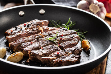 Juicy and grilled beef Rib Eye steak in teflon pan with salt, pepper and rosemary herbs
