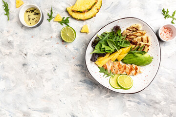 Healthy green vegetables buddha bowl with chicken breast, halloumi, avocado, green rocket salad, lime, sesame and seeds on a white background. Top view