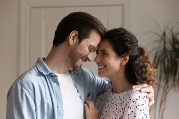 Bonding millennial married family couple touching foreheads, showing tender feelings at home. Loving caring young spouses cuddling, enjoying stress free peaceful weekend time together indoors.