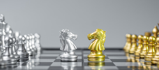 Gold and silver Chess Knight (horse) figure on Chessboard against opponent or enemy. Strategy, Conflict, management, business planning, tactic, politic, communication and leader concept © Jo Panuwat D
