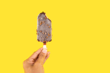 Hand holding a Bite taken Peanuts chocolate ice cream wooden stick on yellow background
