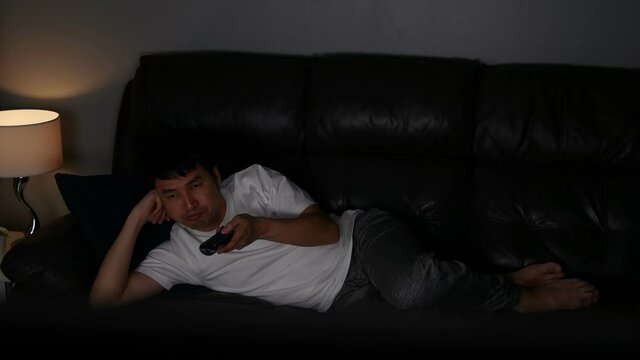 Bored young man watching TV on sofa at night