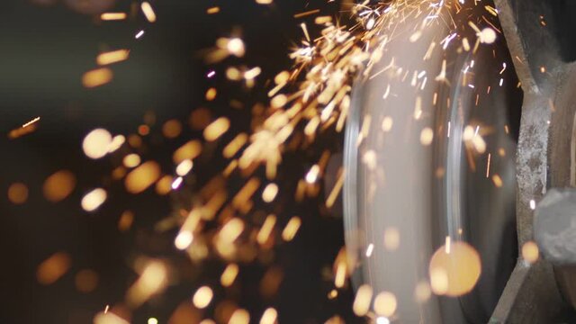 Sparks fly off the grinder machine while sharpening and grinding tools. Slow motion shot. Manual hard work in factory and workshop