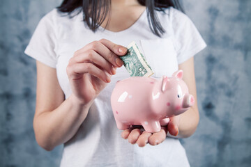 woman throws dollar into piggy bank