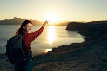woman tourist with backpack shows in the sun sunrise travel adventure