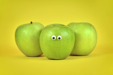 Green apple fruits with funny googly eyes on bright yellow background - obrazy, fototapety, plakaty