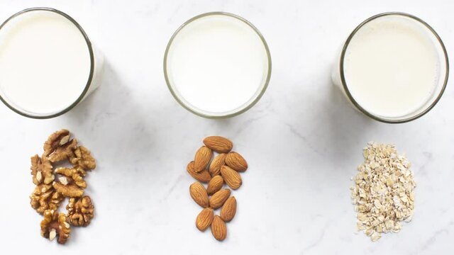 Motion picture of glass of almond, walnut, oat milk on marble background top view. Nut vegan milk. Lactose-free, dairy free milk. Hypoallergenic drink. Healthy diet and nutrition