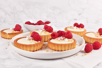 Tartlet pastries with white cream, topped with raspberry fruits and almond sprinkles on white plate