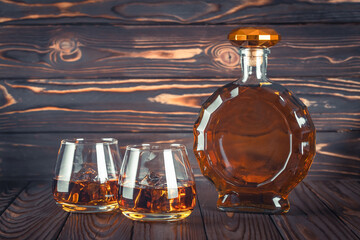 A bottle of whiskey and two glasses on a dark brown wooden table. Transparent yellow alcoholic...