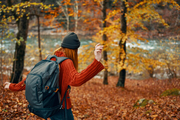 woman hiker with backpack in autumn forest near mountain river and fallen leaves