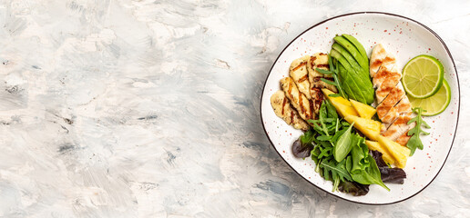 Buddha bowl with pineapple salad, grilled chicken breast, halloumi, avocado, green rocket salad and lime. Long banner format, top view