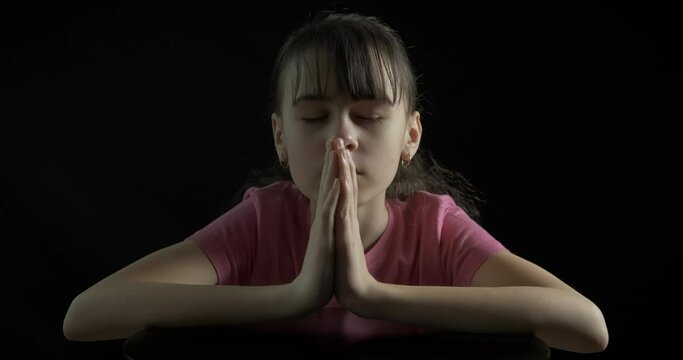 Teen in religion mood. A religion teen hold her hands and pray on the black background.