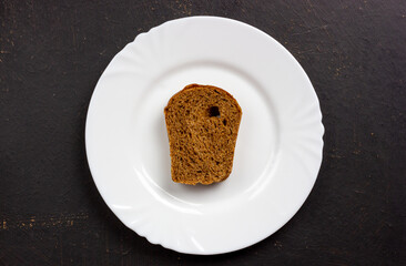 A slice of rye bread on a white plate. Plate with bread on a black background.