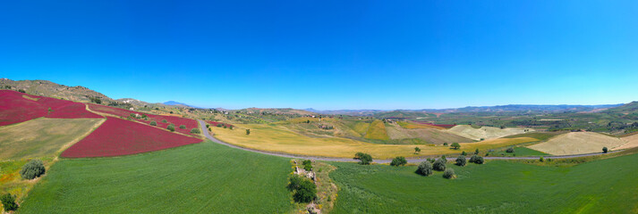 Fototapeta na wymiar 180 degrees aerial photo of the red fields in the heart of Sicily in the Erei mountains. Sulla is a fodder for animals and is sown as bare seed on wheat stubble. Sicilian wheat with a view of Etna.