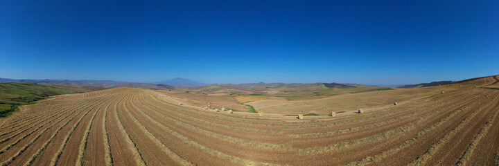 Fototapeta premium 180 degree saerial photo of the wheat fields in the heart of Sicily in the Erei mountains. Sicilian wheat cultivation. Small rural villages of Ramacca and Raddusa. Hay and grain. Etna view.