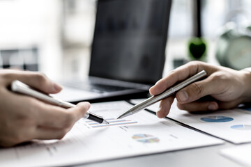 Two business partners are brainstorming on planning, managing and solving company problems, they are pointing at the company financial documents. The concept of business management for growth.