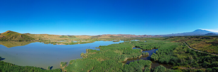 Fototapeta na wymiar 180 degrees aerial photo of the Oasis of Ponte Barca a protected area in the heart of Paternò in Sicily. Wetland that attracts numerous waterfowl. Nesting place of the Sultan chicken. Etna view.