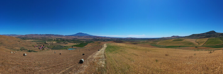 Fototapeta na wymiar 180 degree saerial photo of the wheat fields in the heart of Sicily in the Erei mountains. Sicilian wheat cultivation. Small rural villages of Ramacca and Raddusa. Hay and grain. Etna view.
