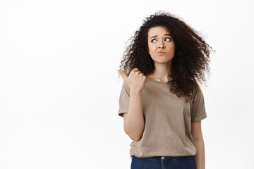 Doubtful young woman pointing and looking left with skeptical disappointed face, dont like this...