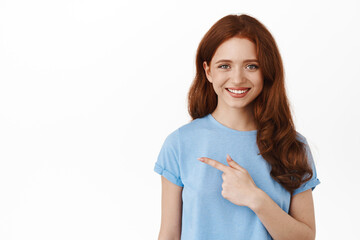 Young woman with red curly hair in t-shirt, pointing finger left, showing advertisement and...
