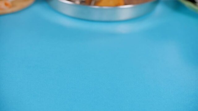 Vegetarian food platter from North India moving slowly in a blue background. Close-up shot of Satvik Indian food served during the Hindu religious festivals - north Indian cuisine