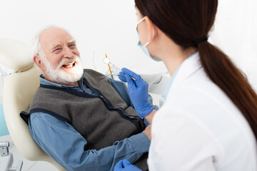 smiling senior man having teeth treatment by dentist in latex gloves in dental clinic.