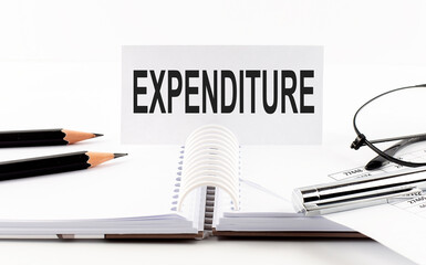 Text EXPENDITURE on paper card,pen, pencils, glasses,financial documentation on table - business concept