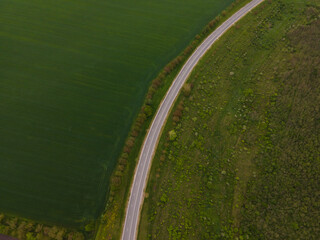 Aerial view of road through rural area. Wheat fields and forest beside asphalt road. Concept of road trip through countryside. Photo from drone.