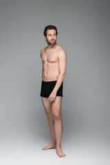 full length of shirtless man in black underwear posing on grey.