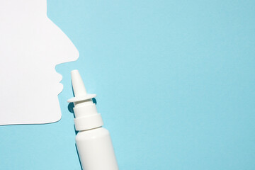 Paper silhouette of a man's head and nasal spray on a blue background. Concept against allergic...