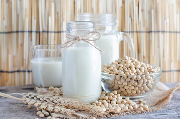 Closed up delicious homemade soybean milk in glass bottle with dry seeds in glass bowl and grunge wooden background, for healthy food cooking or agricultural product concept