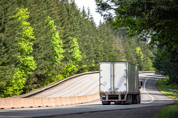Big rig industrial semi truck transporting cargo in dry van semi trailer with safety protective beam on the back running on the curving highway road