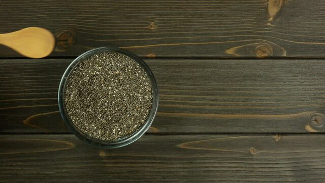 Pour chia seeds into a bowl, copy space. Dark wooden background. Flat lay, top view.