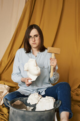 A woman holds a plaster head and a wooden hammer in her hands. The concept of psychology, mental illness, depression, headache