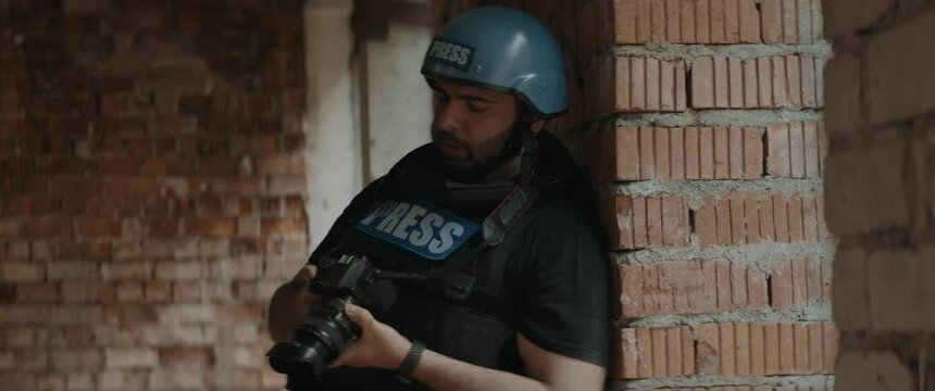 HANDHELD Hispanic male war journalist wearing protective helmet and bulletproof vest gear taking photos during military operation. Shot with 2x anamorphic lens
