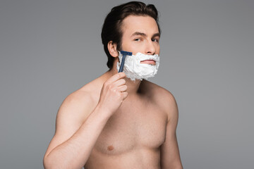 shirtless man with foam on face shaving with safety razor isolated on grey.