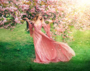 Fantasy happy girl elf princess walks in spring blooming garden. Pink flowers sakura tree green...