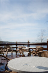 A glass of white wine on a white table on the terrace. Glare from a glass of wine and sunbeams