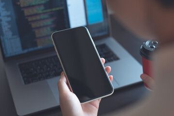 Mockup image, woman holding mobile phone with blank screen template during working on laptop