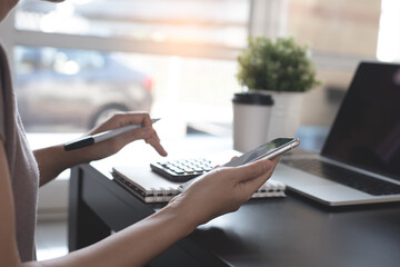Casual business woman, entrepreneur using calculator and mobile phone with laptop computer and cup of coffee on office table at home