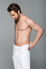 young muscular man adjusting white towel isolated on grey.