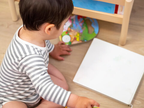 Baby boy in his nursery reading child books. From above view of baby around books for development and learning. Brunette baby wearing bodysuit with a white cover book for mockup.