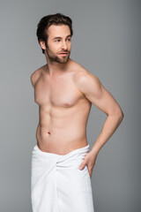 young muscular man wrapped in white towel looking away isolated on grey.