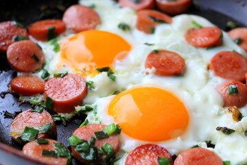 Sausages with green onions and chicken eggs in a pan. Fried delicious meat sausages cut into slices with onions for breakfast.