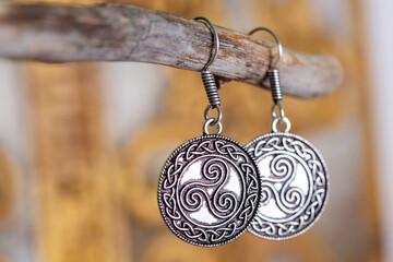 Brass metal earrings in ornamental shape hanging on neutral background